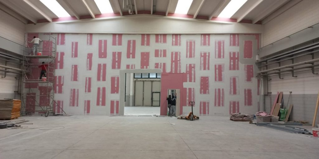 Lavoratori dipingono parete interna edificio industriale.